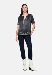 Gray satin top with short sleeves, V-neckline, and decorative embroidery at hem. Paired with dark jeans and white heeled boots.