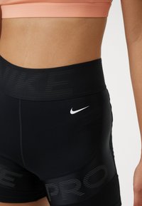 Shorts sportivi neri con una cintura ampia che presenta il marchio "NIKE" in un motivo tonale, accentuati da un piccolo logo bianco dello swoosh Nike.