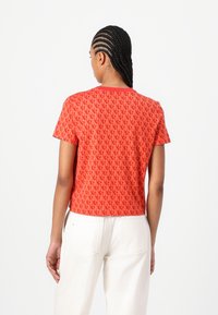 Red short-sleeve t-shirt with a repeating pattern, round neckline, and a cropped design. Paired with white pants, showing a smooth texture.