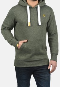 Felpa verde oliva con cordini bianchi, tasca frontale e un logo giallo sul petto. Realizzata in tessuto morbido e strutturato.