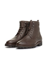 Botas de tobillo de cuero marrón con acabado texturizado, puntera redonda, cordones en la parte frontal y suela de goma con tacos. Presenta ojales de metal y acentos en el cuello.