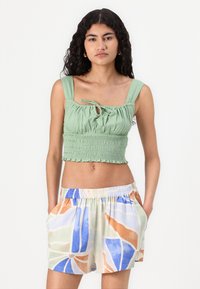 Haut court smocké vert avec de larges bretelles, associé à un short multicolore à motifs dans des teintes pastel de bleu, orange et beige.
