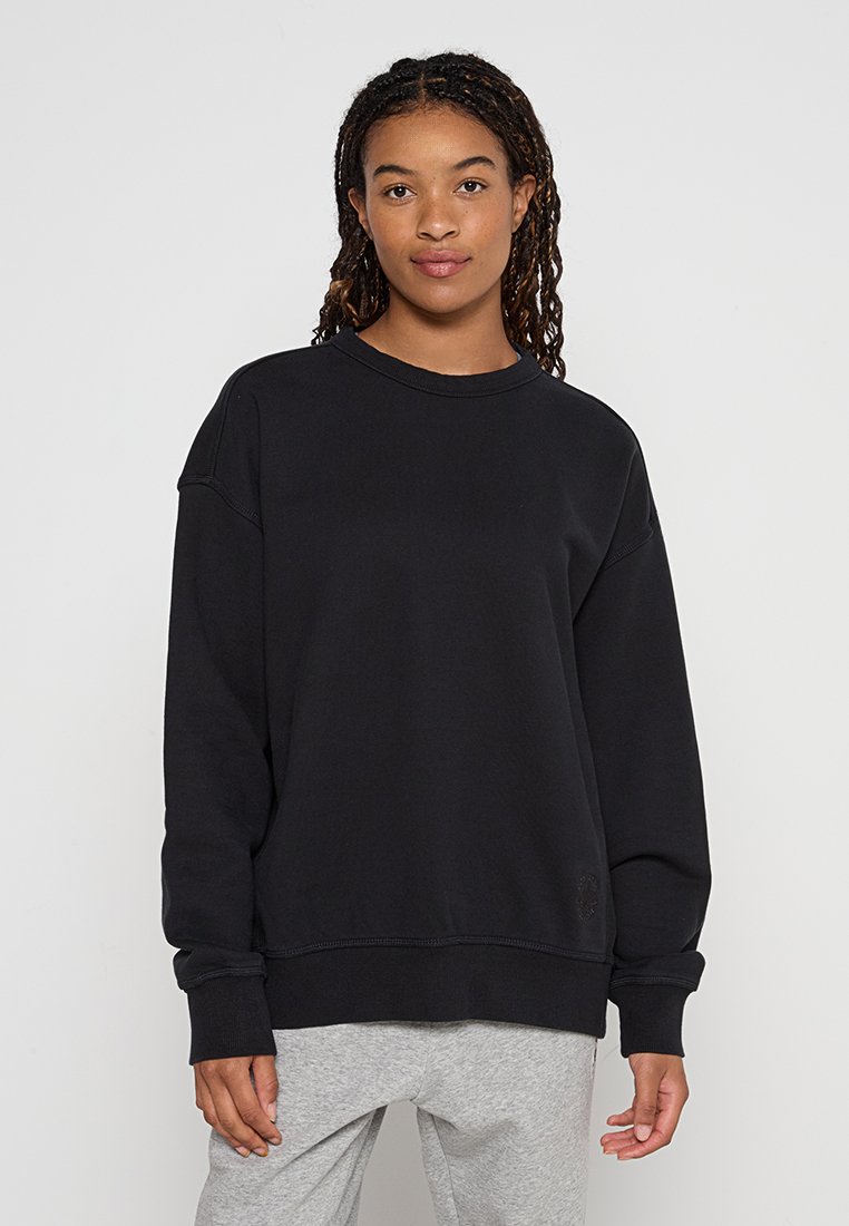 Sweatshirt noir avec un col rond, des épaules tombantes et des poignets côtelés. Fabriqué en tissu doux, avec un petit logo brodé en bas.
