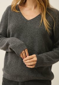 Szary sweter z prążkowanego dzianiny, z dekoltem w kształcie V, długimi rękawami i dopasowanymi mankietami, wykonany z miękkiego materiału. Minimalistyczny design, idealny do warstwowego ubierania się.