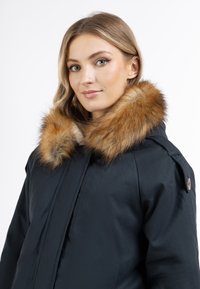 Giacca della marina con un ampio colletto in pelliccia marrone, dotata di chiusura con zip e bottoni laterali, realizzata in materiale liscio e resistente all'acqua.