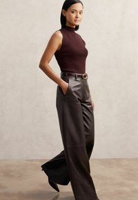 Burgundy ujjatlan felső álló gallérral; magas derekú sötétbarna bőrnadrág, széles szárú; arany övcsat; sima textúra.
