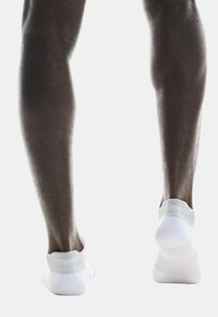 Weiße Knöchelsocken aus einem weichen, dehnbaren Material mit ribbeliger Textur am Bund, auf dunkler Haut gezeigt. Sichtbar von hinten.