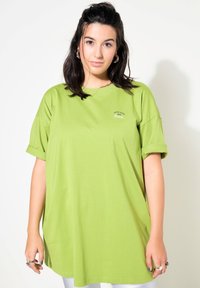 Grøn oversized T-shirt lavet af bomuld, med opsmøgede ærmer og et lille trykt logo på brystet. Glat tekstur og afslappet pasform.