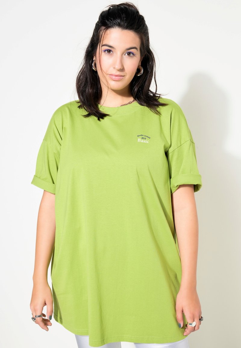 Grøn oversized T-shirt lavet af bomuld, med opsmøgede ærmer og et lille trykt logo på brystet. Glat tekstur og afslappet pasform.