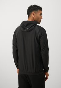 Zwarte sportjack met capuchon, met textuurelementen op de schouders, elastische zoom en een lichtgewicht, gladde stof.