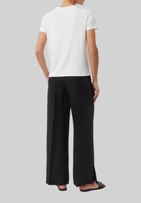 White cotton t-shirt with short sleeves, paired with black wide-leg trousers featuring side slits and flat sandals.