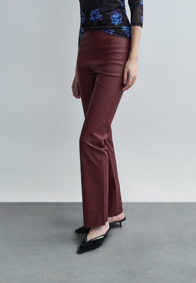 Burgundy leather flared pants with a smooth texture. Paired with black pointed mules with slender straps and a small heel.