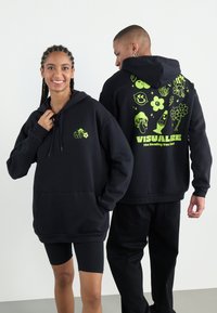 Black hoodie with front pocket, featuring neon green graphic designs, including flowers and symbols, and the word "VISUALIZE" on the back.
