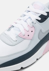 Nike tenisice s gornjim dijelom od bijele kože, svijetlosivim, ružičastim i mornarskim plavim naglascima, teksturiranim panelima i ravnim bijelim vezicama.