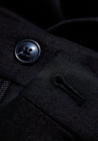 Zwarte stof met een gladde textuur, met een grote ronde knop en een klein lusdetail, dat de naaikunst en het ontwerp benadrukt.