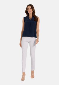 Navy ärmellose Bluse mit einem Keyhole-Ausschnitt und Bindedetail, kombiniert mit weißen Slim-Fit-Hosen und transparenten Sandalen. Glatte Textur.