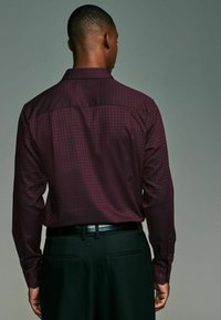 Bordeauxfarbens Langarmhemd mit geometrischem Muster, ausgestattet mit einem Button-Down-Kragen und glatter Textur, kombiniert mit dunklen Hosen.