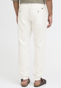 White linen pants with elastic cuffs, two back pockets, and subtle stitching details. Paired with slip-on brown sandals.