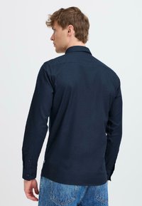Camisa de manga larga azul marino con cuello, puños abotonados y una tela texturizada. Combinada con unos jeans de mezclilla azul claro.