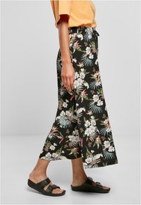 Sorte blomstrete bukser med elastisk midje, prydet med et livlig mønster av hvite og pastellfargede blomster, kombinert med mørke sandaler.