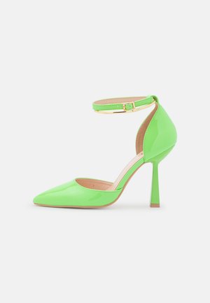 Zapato de tacón alto verde lima brillante con punta puntiaguda y correa en el tobillo con una pequeña hebilla dorada, sobre fondo blanco.