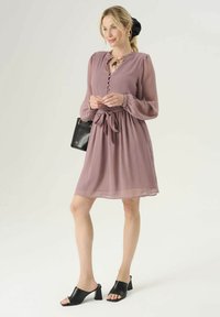 Krótka sukienka w kolorze mauve z krótkim rękawem posiada zapięcie na guziki przy dekolcie, elastyczną talię ze sznurkiem i zwiewną, przezroczystą fakturę, zestawiona z czarnymi klapkami na obcasie.
