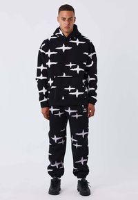 Sudadera negra con capucha y pantalones a juego que presentan un patrón de explosión de estrellas en blanco. Fabricado con una tela suave, tiene un corte relajado y capucha ajustable.