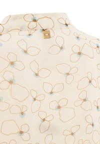 Cremefarbener Stoff mit einem zarten floralen Muster in Hellblau und Braun, mit einem kleinen goldenen Markentag Nähe der Kragennaht.