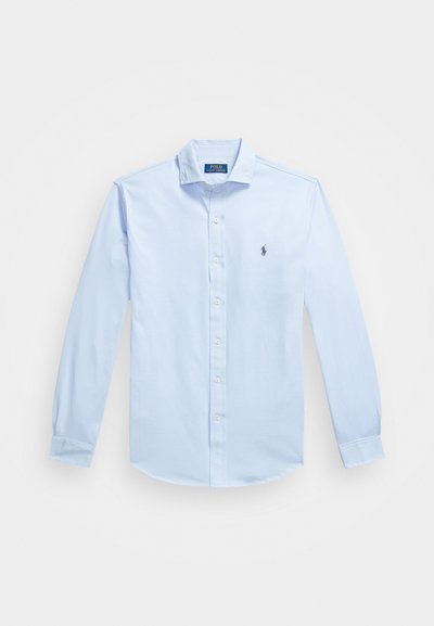 Camisa de botão de manga longa em tecido de algodão, na cor azul claro. Possui um colarinho clássico, um único bolso no peito com um pequeno logótipo bordado.