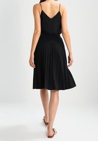 Mustat laskostetut mekko, jossa on ohuet hihnat, V-pääntie ja keskipitkä helma, joka on varustettu virtaavalla muotoilulla ja sileällä kankaan pinnalla.