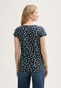 T-shirt marine à manches courtes, avec un motif de points vert menthe, encolure ronde et tissu doux. Associé à un jean bleu.