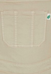 Material bej cu un buzunar dreptunghiular cusut, având cusături verticale și o mică etichetă albă cu un simbol de frunză verde pe partea dreaptă.