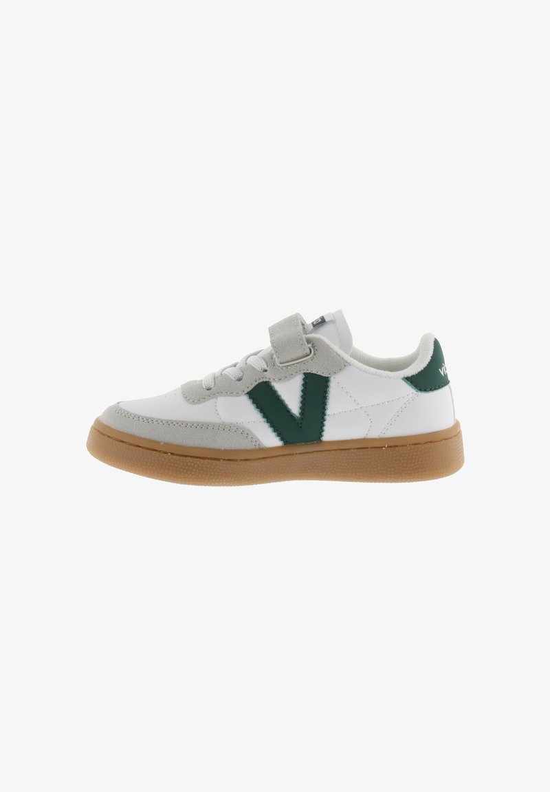 Zapatilla blanca con logo en V verde, acentos de gamuza gris y suela de goma beige. Presenta una correa ajustable y un diseño clásico de zapatilla de tenis.