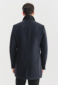 Czarny wełniany płaszcz w ciemnoszarym kolorze z czarnym kołnierzem, wyraźnie zarysowanymi ramionami i dopasowanym krojem, z czystym szwem na plecach i gładką teksturą.