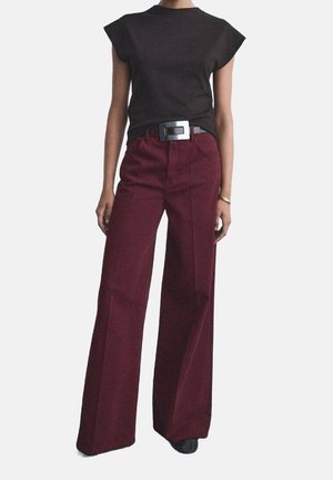 Woman modeling sleeveless black top tucked into high-waisted wide-leg burgundy pants with black belt and rectangular silver buckle.