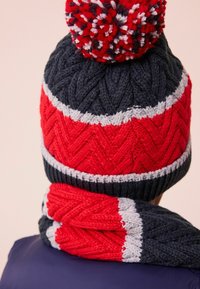 Knitted hat and scarf set in navy, red, and gray. Hat features a pom-pom and herringbone pattern; scarf has matching design elements.