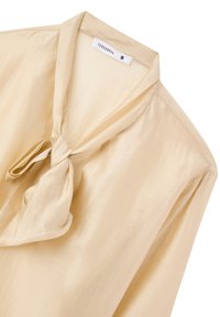 Blusa crema realizzata in tessuto morbido, con un fiocco al colletto, maniche lunghe e una vestibilità leggermente ampia per il comfort. L'etichetta mostra "Terranova" e la taglia S.