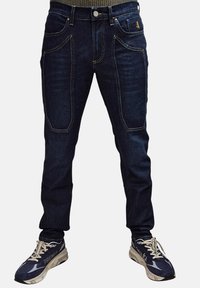 Jeans in denim blu scuro con tasche frontali e cuciture a contrasto. Abbinati a sneakers navy e beige dal design elegante.