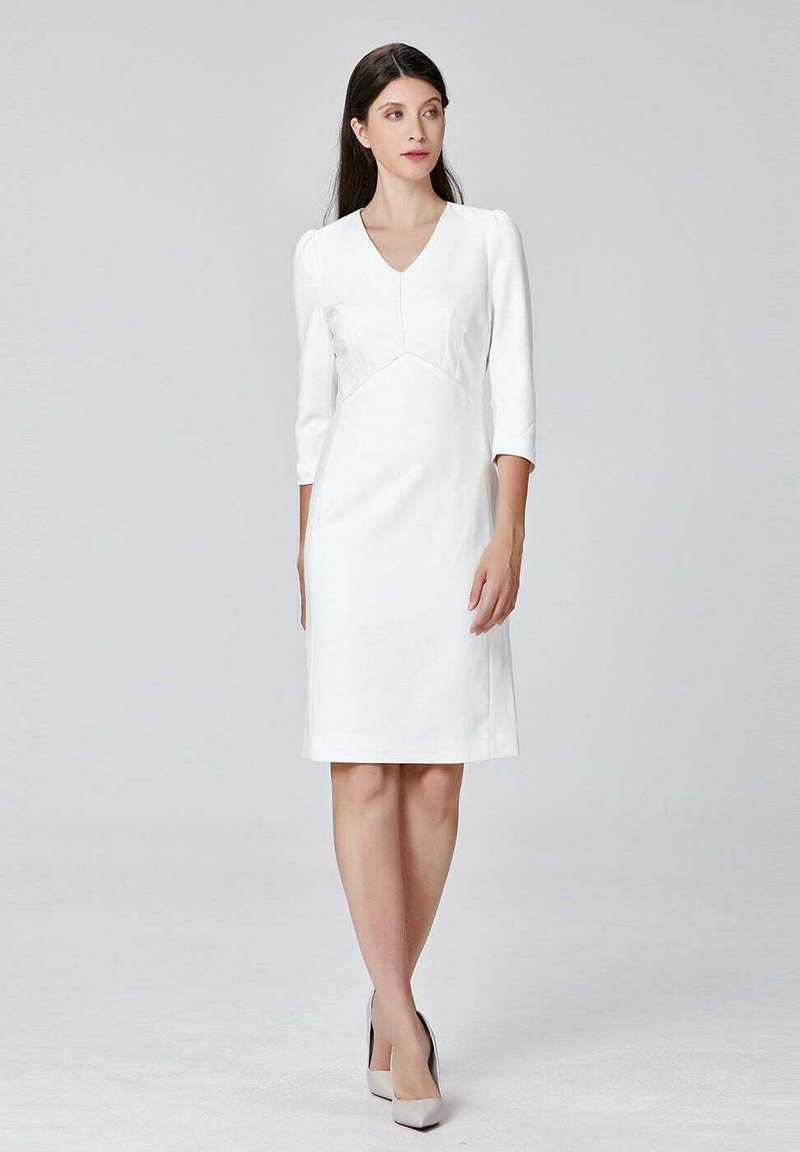 Robe blanche, longueur genou, avec un col en V, des manches trois-quarts et un corsage ajusté. Tissu lisse avec des détails de couture subtils.