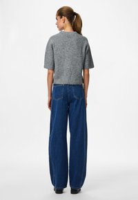 Pilkas trumpas rankovėmis megztinis su apvalia iškirpte, derinamas su plačiomis mėlynomis džinsinio audinio kelnėmis. Lygus paviršius ir laisvas fasonas.