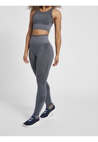 Szary sportowy zestaw składa się z dopasowanego biustonosza i legginsów z wysokim stanem z teksturowanymi akcentami. Obuwie ma siateczkowy wzór w niebieskich odcieniach.