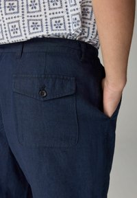 Mørkeblå linnedbukser med en baglomme med knap. Slim fit med en tekstureret stof. Håndplaceret i forlommen.