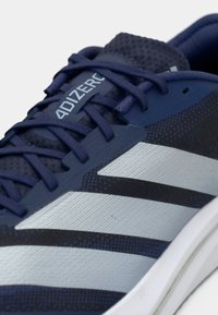 Κοντινή λήψη του παπουτσιού τρεξίματος Adidas 4D IZER σε σκούρο μπλε ναυτικό χρώμα, που δείχνει τα κορδόνια, το αναπνεύσιμο δίχτυ και το λευκό σχέδιο ρίγας στο πλάι.