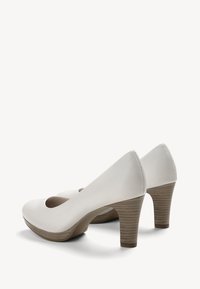 Chaussures à talon haut en cuir blanc avec un bout rond, mettant en avant un design découpé et un talon en bois texturé brun.