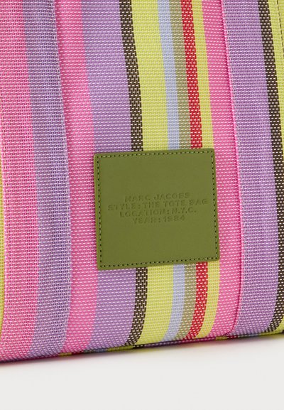 Sac cabas tissé coloré avec des rayures verticales roses, jaunes, marron et violettes, écusson vert avec texte embossé sur le devant.