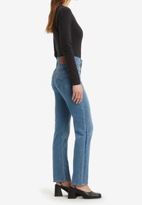 Blå denim raka jeans med hög midja, med en läderlapp på baksidan och utsmyckade bakfickor. Bärs tillsammans med en svart långärmad topp.