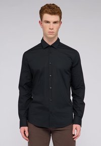 Camisa negra de manga larga abotonada con cuello, textura suave, botones negros y un diseño de corte ajustado. Sin patrones ni acentos visibles.