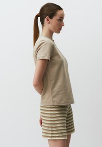Beige Baumwoll-T-Shirt mit kurzen Ärmeln, kombiniert mit gestreiften Strickshorts in Beige und Hellbraun. Glatte Textur mit legerem Schnitt.