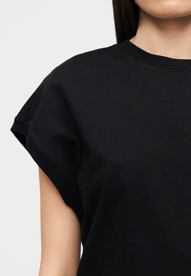 T-shirt en coton noir avec un col rond et des manches courtes retroussées. Texture lisse avec une coupe décontractée.