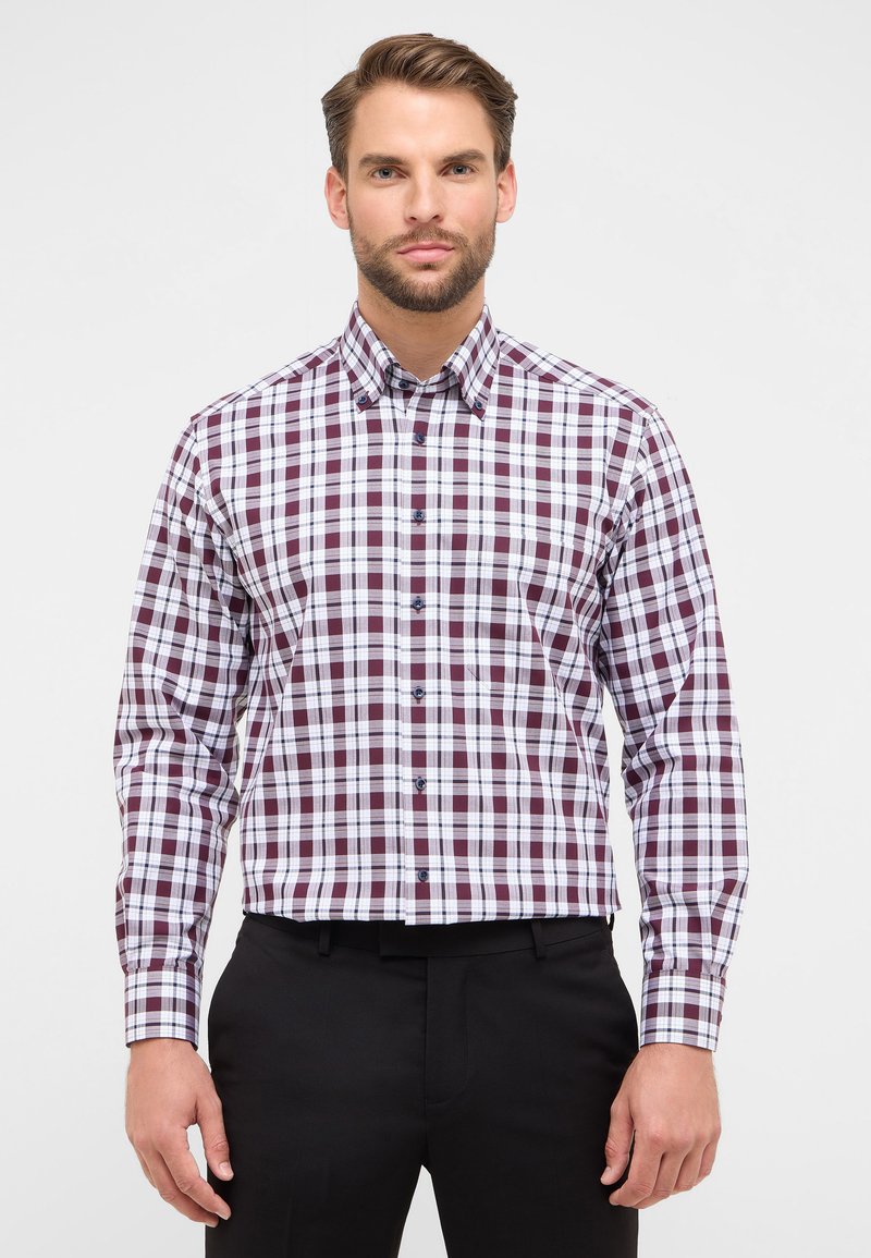 Camicia a maniche lunghe con bottoni, caratterizzata da un motivo a quadri burgundy e bianco, con colletto e bottoni blu, su uno sfondo di pantaloni neri.